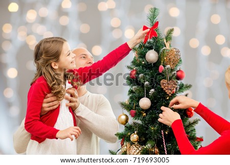 family, holidays and people concept - happy mother, father and daughter decorating christmas tree over lights background