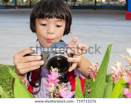 Asian pretty girl child holding camera and take a photo of beautiful flower on blurred background 