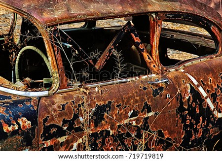 rusted hulk of large american car with remnants of black paint and chrome strips abandoned on a South Dakota farm Royalty-Free Stock Photo #719719819