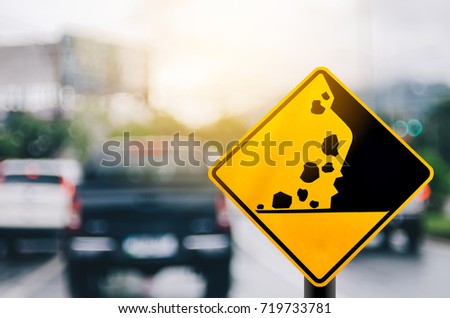 Falling stone warning traffic sign on blur road with colorful bokeh light abstract background. Copy space of travel and transportation concept. Vintage tone filter effect color style.