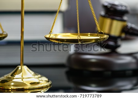 Legal office of lawyers, justice and law concept : Brass scales of justice with blurred wooden judge gavel or wood hammer and a soundboard on  judiciary desk in a courtroom with thick law books behind Royalty-Free Stock Photo #719773789