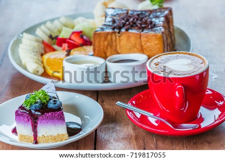 Heart latte art hot coffee in red cup, blueberry and other cake on the wooden table as love and dessert concept