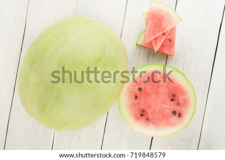 Three slices beside whole fresh ripe watermelon and one half of watermelon on old wooden rustic white table