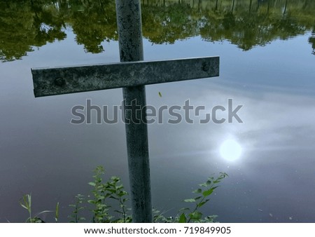 Close up Christian cross with sun reflection on water pond surface