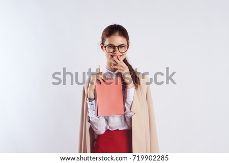 a young teacher in a jacket and glasses holds an orange notebook on a light background                               