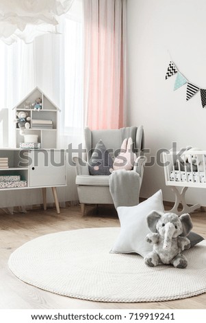 Grey elephant toy and star pillow on white round carpet in baby's room with grey armchair and cupboard