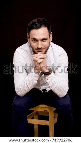 Portrait of a handsome guy on black background. Thoughtful attitude. Businessman sitting with crossed hands.