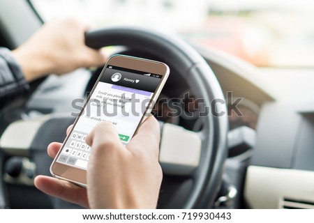 Texting while driving car. Irresponsible man sending sms and using smartphone. Writing and typing message with cellphone in vehicle. Holding steering wheel with other hand. Royalty-Free Stock Photo #719930443