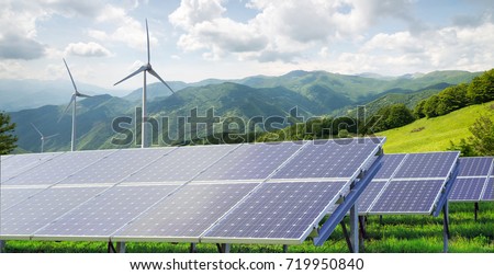 solar panels with wind turbines against mountanis landscape against blue sky with clouds panorama Royalty-Free Stock Photo #719950840