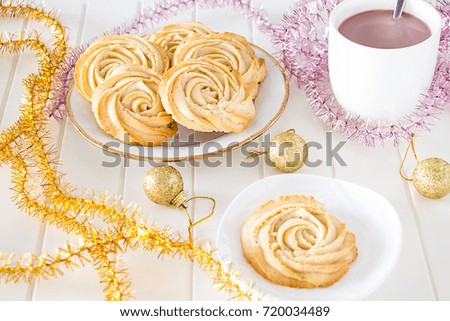 Christmas concept. Round shortbread cookies roses form and Cup hot chocolate. Vintage white plate. Multicolor tinsel. White background wooden.