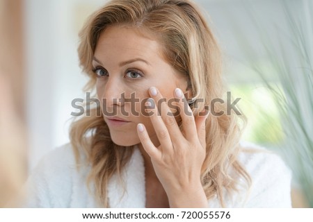 Portrait of attractive blond woman applying anti-aging cream Royalty-Free Stock Photo #720055576