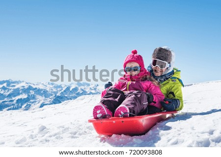 Happy little brother and cute sister enjoying sleigh ride. Smiling children sitting on the sled. Children play with bobsled outdoors in snow. Winter vacation concept.