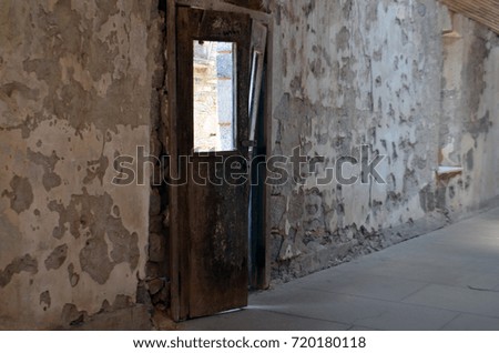 Old rusty weathered door in peeling paint hallway corridor of abandoned historical jail