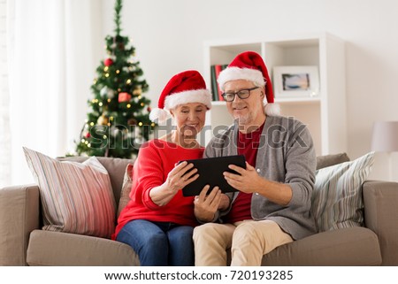 christmas, holidays and people concept - happy smiling senior couple in santa hats with tablet pc computer at home