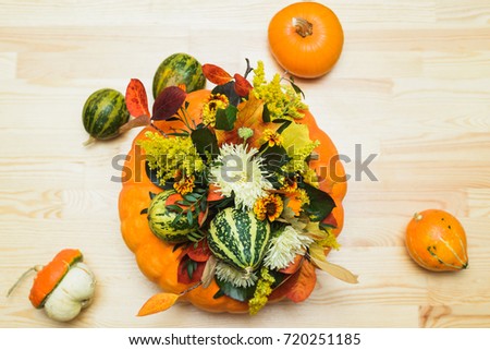 autumn bouquet of decorative pumpkins, flowers and leaves in a vase of orange pumpkin on a wooden table