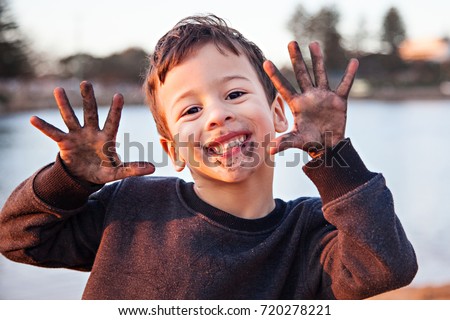 A head and shoulders photo of a handsome, smiling, dark haired, brown eyed little boy excitedly showing off the dirt on his face and hands after playing outdoors. Royalty-Free Stock Photo #720278221