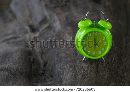 Green table clock on wooden stump with nature background, selective focus 
