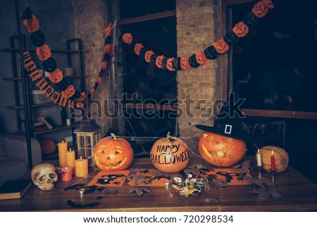 Preparation for halloween, cutted pumpkin, fall leaves, spider web net, skull, cap of witch, bowl with candies on top of wooden table. Ready for feast in mystery interior. Concept of hallows eve