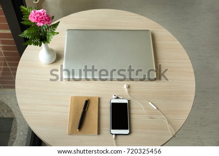 Cell phone with earphones and laptop and notebook and pen with flower on wooden table