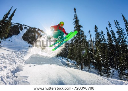 Skier freerider jumping from a snow ramp in the sun on a background of forest and mountains. Royalty-Free Stock Photo #720390988