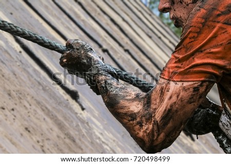 Mud race runners, defeating obstacles by using ropes Royalty-Free Stock Photo #720498499