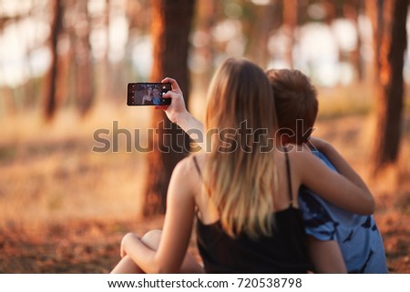 Adorable romantic couple of teen boyfriend and girlfriend taking a selfie on a blurred autumn forest background. Copy space.