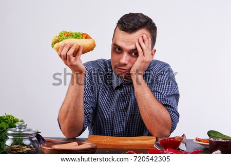 Young man in a blue shirt eats a hot dog, isolated on a white background.