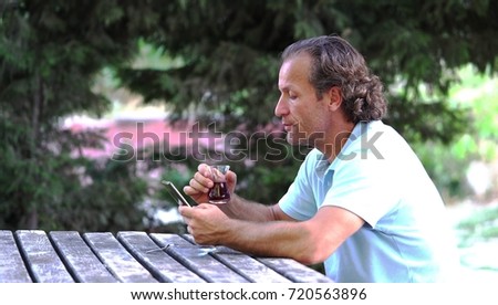 Portrait of a male sitting on the bench and drinking coffee or tea outdoors