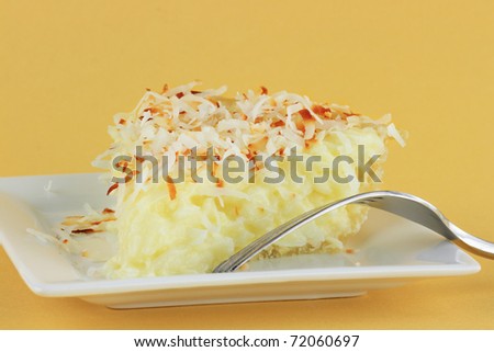 Slice of homemade coconut cream pie against a yellow background.