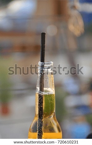 A flavored yellow drink with a black drinking straw in a bottle.