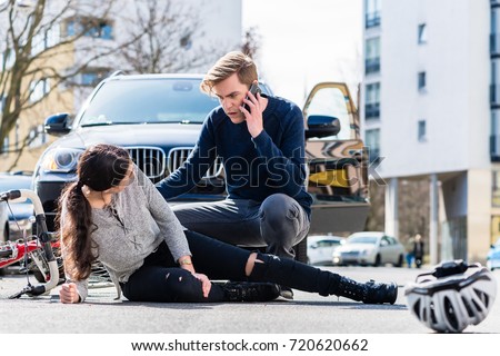 Full length view of a worried young driver calling the ambulance after hitting and injuring accidentally a female bicyclist on a city street 