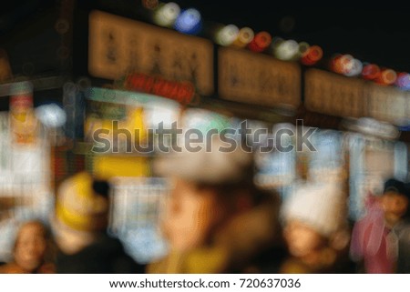 Defocused sillhuettes of Illuminated Christmas fair kiosk market stall with loads of bootles with vin chaud - hot mulled wine and customers waiting in queue 