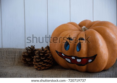 Orange Halloween pumpkin. Halloween holiday concept.Autumn background with pumpkin. Girl is drawing a smile in a pumpkin.Autumn decoration of pumpkin and cones.