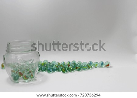 Many glass marble balls and the colorless pot on the left of the picture, isolated on white background 