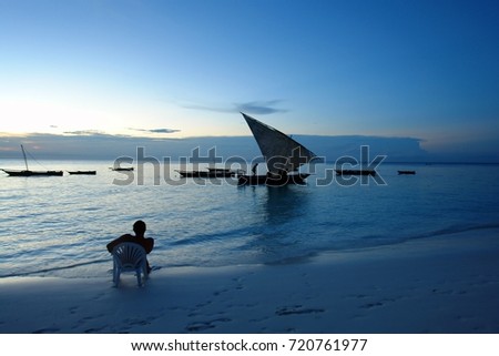 Man sitting on chair looking into sea at sunset on Zanzibar beach, Tanzania