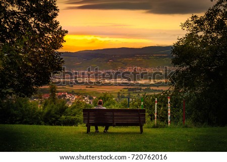 Man sitting on a bench and looking over a plain in Rheinhessen in the sunset