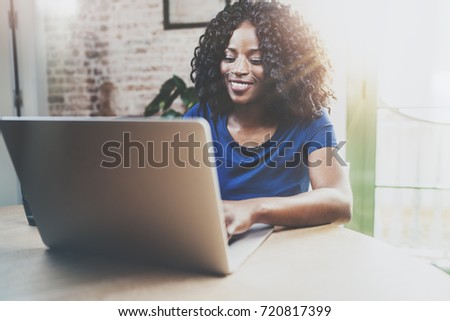 Smiling african american woman using laptop while sitting at wooden table in the living room.Horizontal,blurred background Royalty-Free Stock Photo #720817399