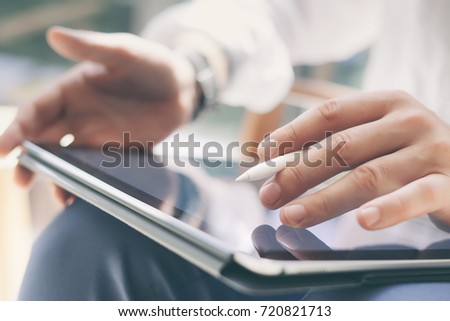 Closeup view of coworker holding digital tablet on hand and using electronic pen while working at office.Pointing tablet screen.Blurred background.Horizontal