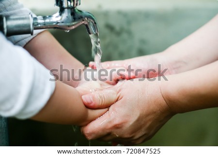 Parent is holding hand and washing his baby's hand./Closeup photo of woman washing hands in a city fountain