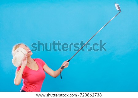 Technology, modern photography, confidence conept. Happy attractive adult blonde woman with sun hat taking picture of herself with smartphone on selfie stick.