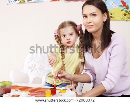 Child painting in preschool. Teacher help by little girl.