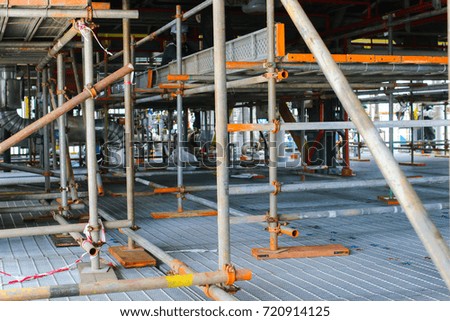 Scaffolding installation on gratings with process structures of refinery petrochemical plants in the background.