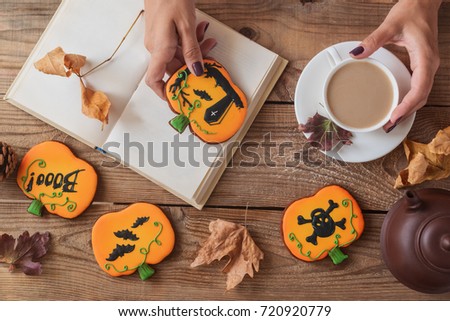 Halloween cookies on the table. Women's hands, a cup of coffee, a book and glasses

