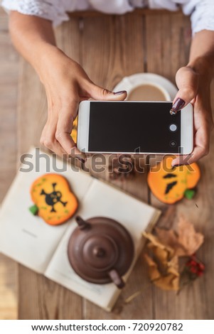 Female hands photographing a table with Halloween biscuits and coffee on their phone


