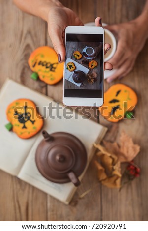 Female hands photographing a table with Halloween biscuits and coffee on their phone


