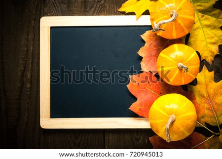 Thanksgiving day background. Autumn pumpkins and leaves around chalkboard on wooden table. Top view copy space.