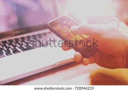 Stock exchange concept, hand holding mobile and note in laptop. Selective focus and toned image, free space for text.
