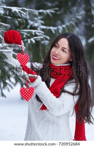 Happy young woman decorating christmas tree. Winter outdoor portrait of girl in sweater, red glove and scarf