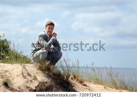 Teenage boy sits on sand dune - rest on beach - cloudy blue sky and sea background