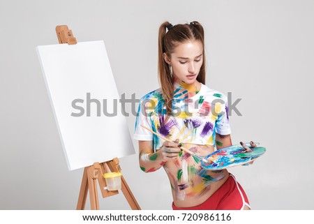 beautiful young woman artist soiled in colorful paint draws on canvas.